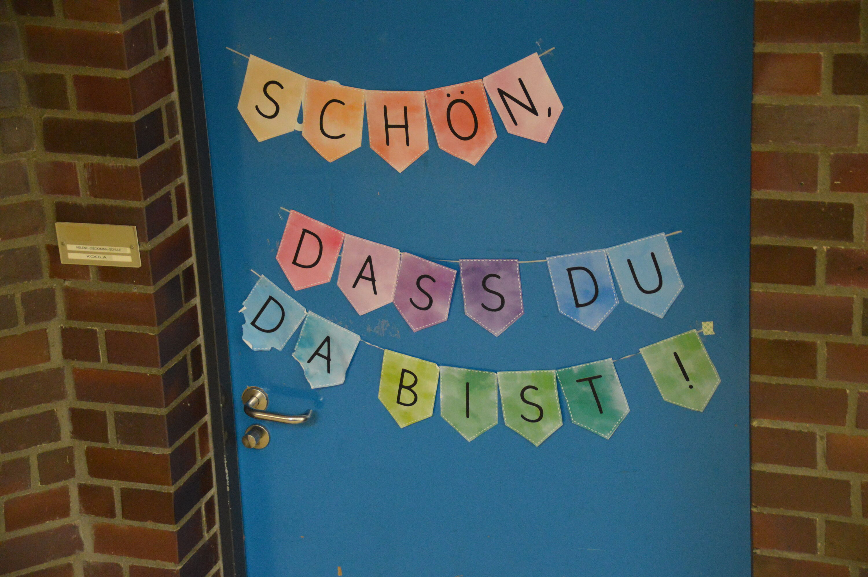 Tür mit einem bunten Türschild, auf dem steht:" Schön, dass du da bist."